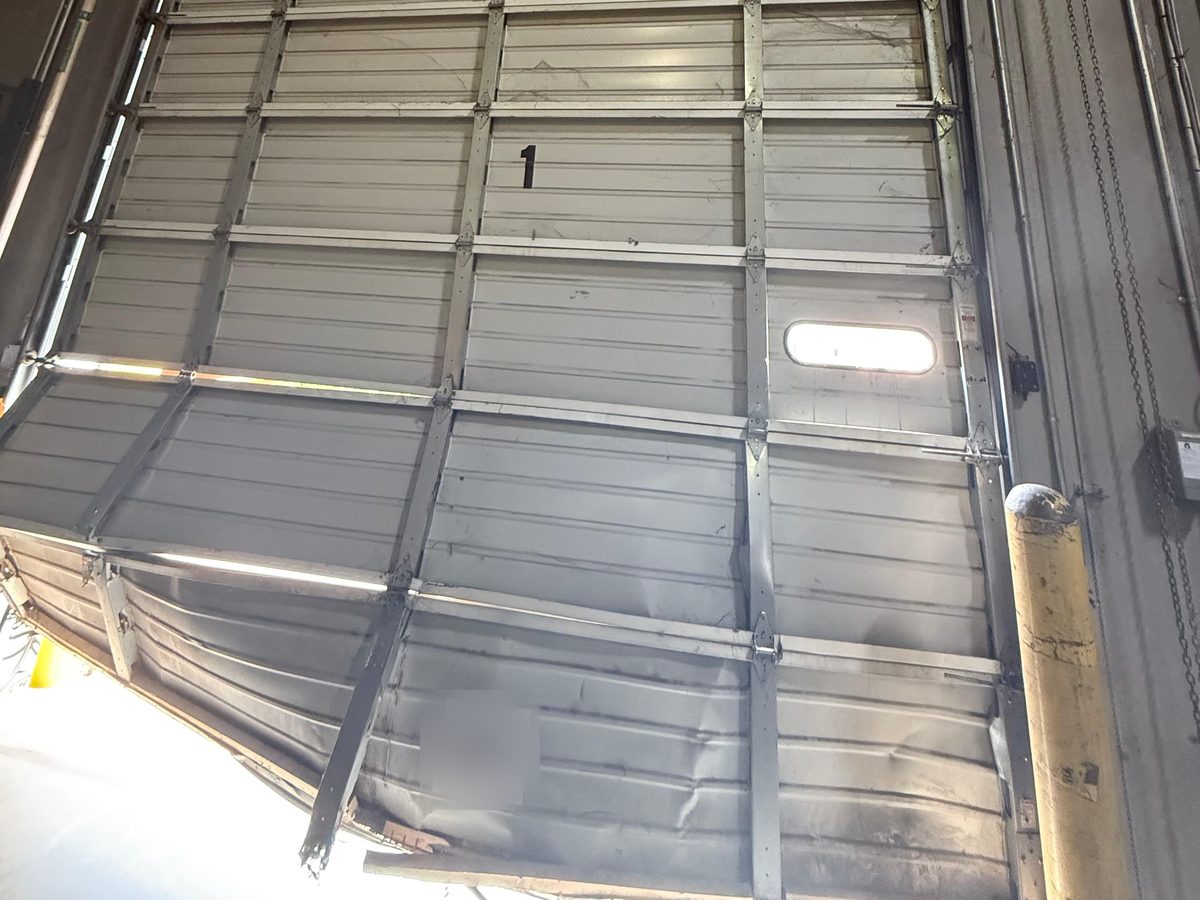 Door seen from inside with the bottom sections bent and pushed out of line – Joy Garage Services job