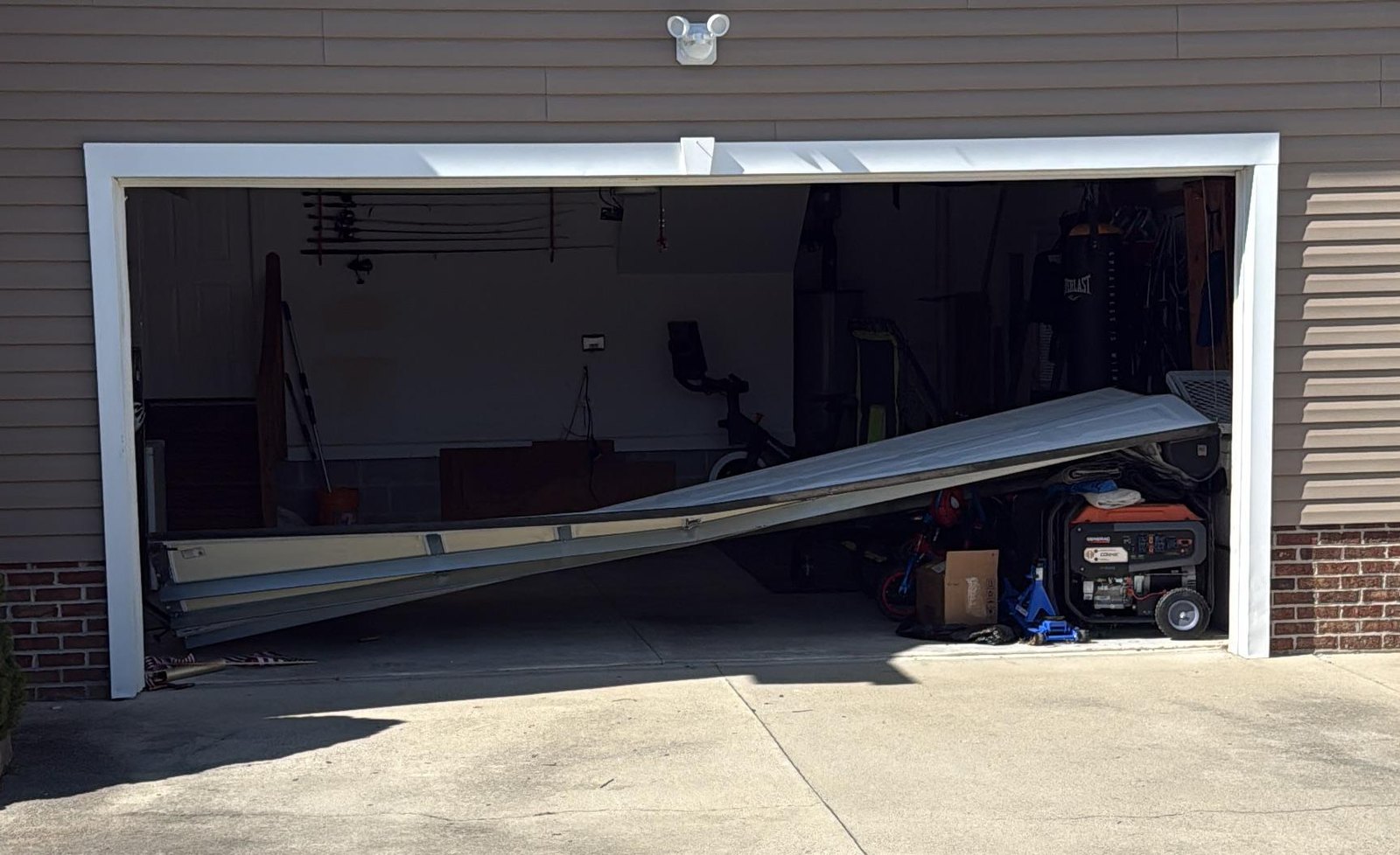 Severe case: a residential garage door collapsed and bent off its tracks, lying across the open garage doorway – Joy Garage Services job