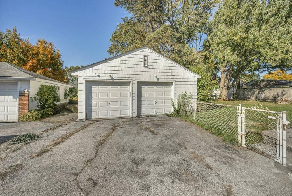 Detached white two-door garage with a cracked driveway