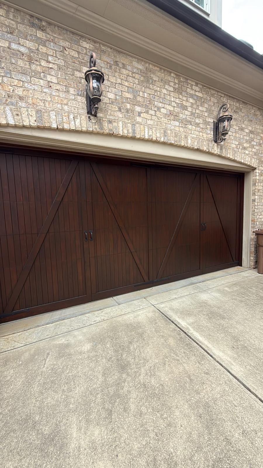 Dark wood carriage-style double garage door with X-brace trim and black handles on a brick house