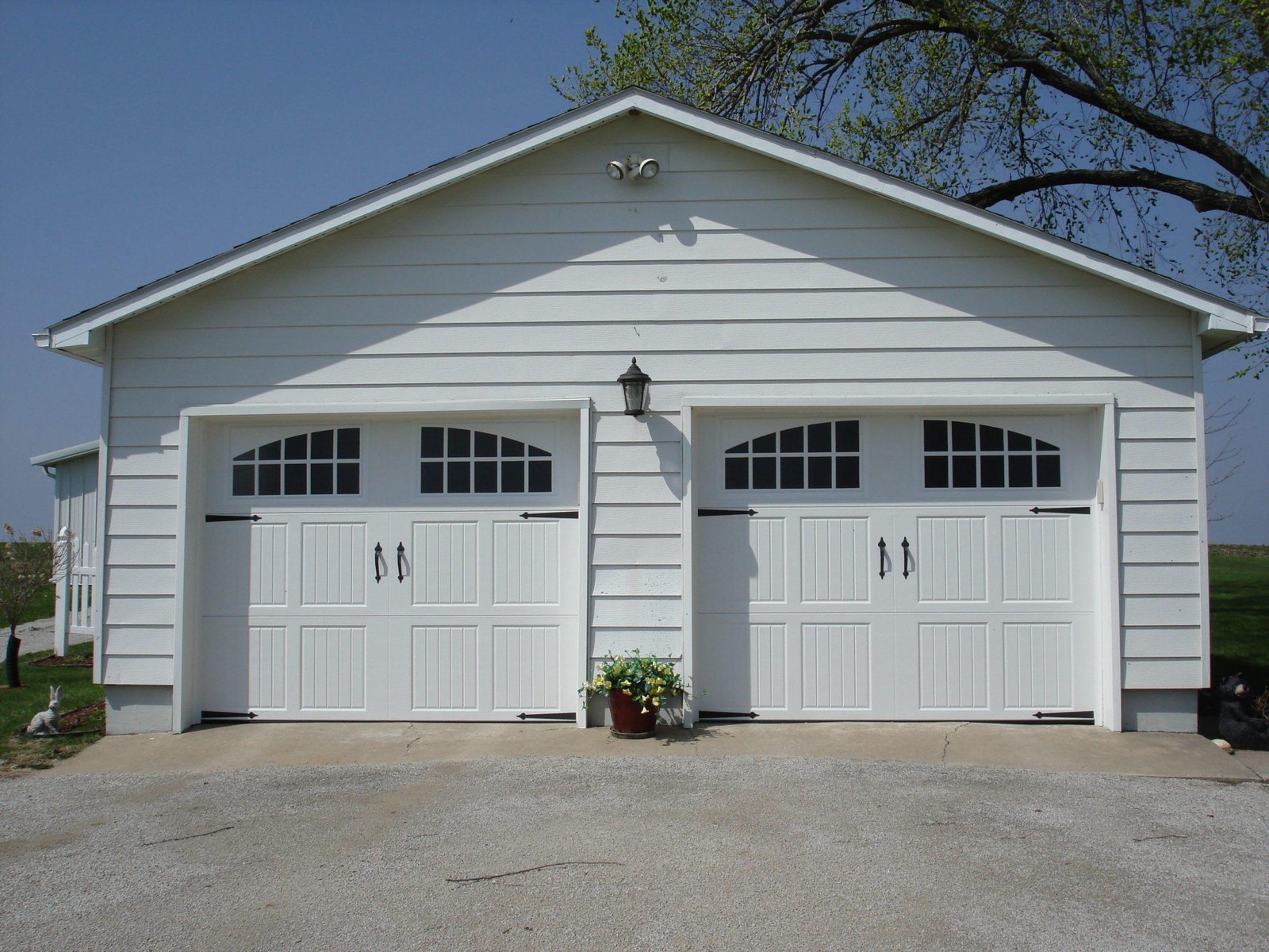 Two white carriage-style garage doors with arched windows on a white garage building