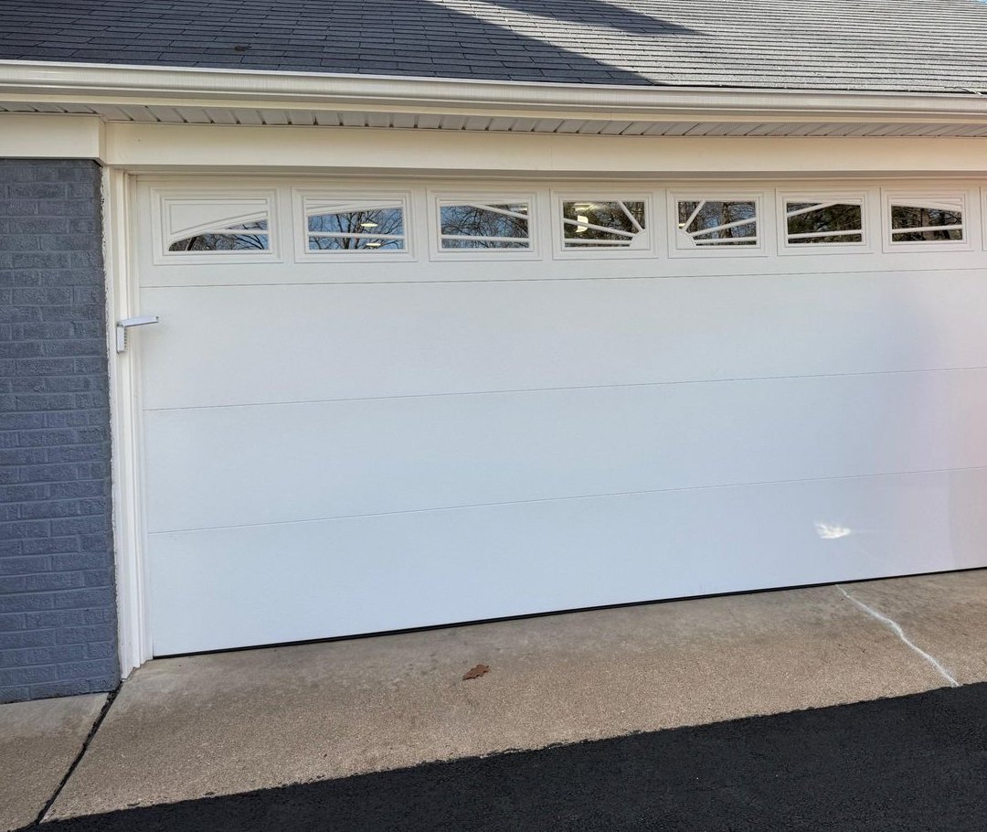 White garage door with a row of sunburst-style windows set in gray brick